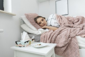 A sick teenager is lying on the bed. In front of the bed is a white table with a plate full of