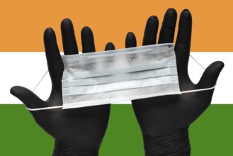 Doctor holds face mask in hands in black medical gloves on background colors National Flag of India