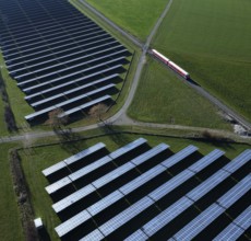 Red local railway runs on a non-electrified railway line next to a solar park through green