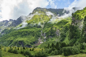 Imposing green mountains with waterfalls and clouds, offering a majestic view of nature,