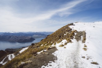 A mountain path with snow offers an impressive view of a lake and mountains, Roys Peak, Wanaka, New