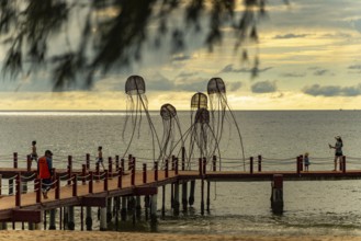 Families walking on a pier with jellyfish sculptures at a peaceful ocean sunset, sun, sunset,