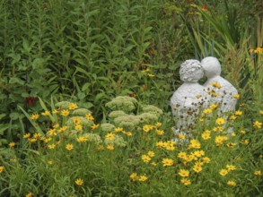 Stone sculpture in the middle of a blooming garden landscape with yellow flowers and green foliage,