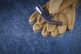 Pair of leather protective gloves with metal claw hammer on scratched metallic background