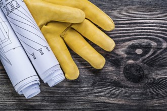 Set of leather protective gloves rolled engineering drawings on wooden board construction concept