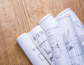 Little pile of white blueprints on brown wooden board close up view