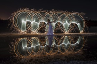 Woman posing for lightpainting photos with bright lights in the dark. Reflection in the water