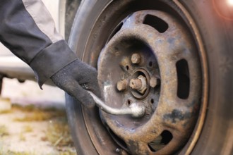 Gloved hand using a wrench on a rusty wheel, focusing on vehicle repair
