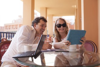 Young couple relaxing over coffee on a balcony sitting at a glass table smiling as they lean close