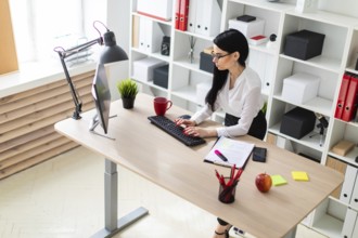 A young girl with glasses, wearing a white blouse and black trousers, works in the office. The girl