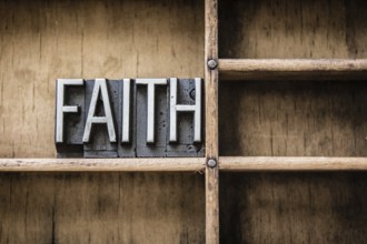 The word FAITH written in vintage metal letterpress type sitting in a wooden drawer