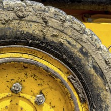 Extreme close up of tire bulldozer, yellow and covered with mud