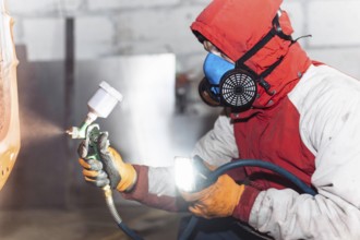 A person in protective gear using a spray gun, illuminating the work area