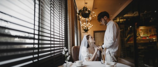 Bride and groom sharing a romantic moment by the window in a softly lit cafe