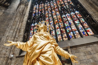Statue of Madonna in gold against the background of a stained glass window in the Duomo. Milan,