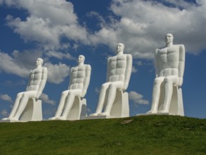 Four large white sculptures of seated men on a green meadow under a blue sky with clouds, esbjerg,
