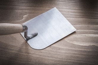Metal bricklaying trowel on vintage wood board close up view