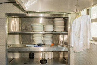 Stacks of dishes on stainless steel storage rack in abandoned resort restaurant kitchen