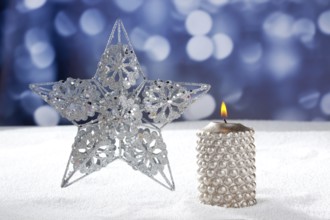 Christmas card of silver star and candle on snow and blue background