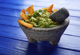 Guacamole with nachos avocado in Mexican molcajete on blue wood table