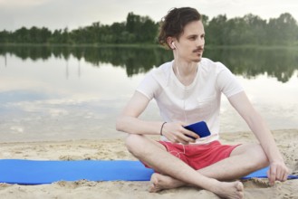 Young man walking near beautiful bay using phone and headphones for communicate with friends and