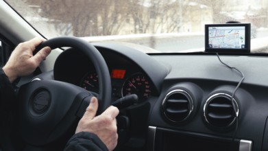 Close-up shot of a man driving a car in winter city. GPS device on the dashboard helps him to find