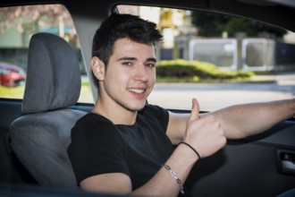 Happy young man or teenager doing thumb up sign while driving car and smiling at camera