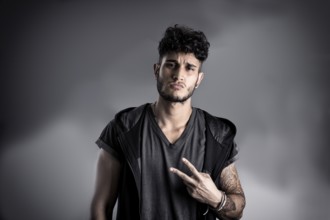 Portrait of handsome young man in dark t-shirt on black background, doing Victory sign with fingers
