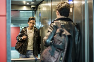 Handsome young man leaning against mirror inside an elevator or lift, looking at camera