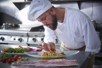 Chef garnishing flower in ceviche dish with hands at stainless steel kitchen