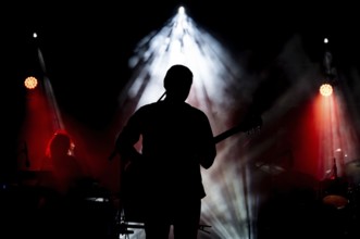 Musician playing guitar performing on stage under spot light. Silhouette of a music artist and band