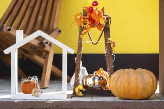 Autumn decor on porch of yellow house outside of pumpkin, lantern, garlands and figure of home and