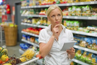 A woman is overwhelmed by the large selection in a supermarket while shopping. Austria