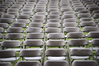 Parallel rows of empty folding chairs in a meadow in front of a concert