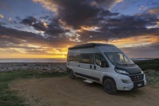 A gray camper van parked on the shores of the Gulf of Taranto in Apulia at sunset