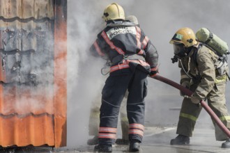 Firefighters extinguishing fire from fire hose, using firefighting water-foam barrel with
