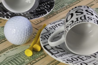 Two empty coffee cups and golf equipments lying on US dollar banknotes
