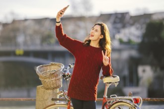 A beautiful young woman with a retro red bicycle is making a photo of herself in the old city of