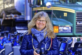 Woman with camera smiling in front of a row of Citibikes and a lorry, Manhattan, New York, USA,