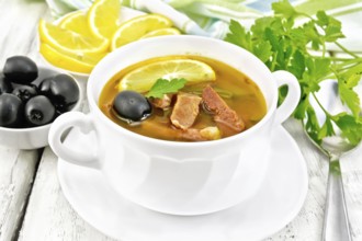 Soup saltwort with lemon, meat, pickles, tomato sauce and olives in a white bowl, towel, parsley on