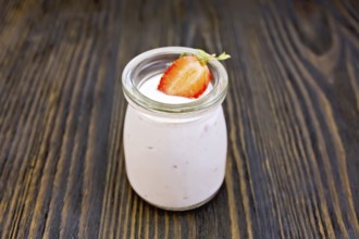Yogurt with strawberries in a glass jar on a wooden boards background