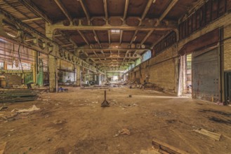 Wide, abandoned factory hall with debris on the floor and visible ceiling construction, The