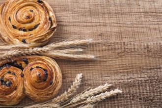 Golden wheat ears fresh-baked buns with raisins on oaken wooden board food and drink concept