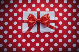 White gift box with knot on polka-dot red fabric holidays concept