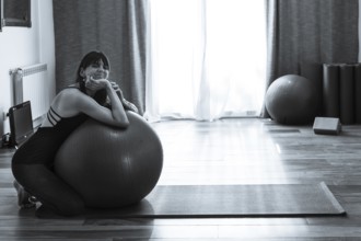 A woman leaning on a fitness ball while she looks at the camera