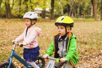 Portrait of screaming preschool girl in protective helmet riding balance bike outdoors at the park.
