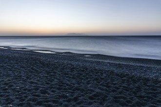 Morning atmosphere, sunrise over the sea, view from the lava beach to the island of Anafi, long