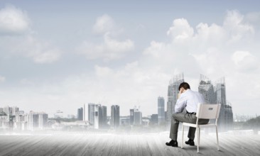 Businessman sitting on an office chair with his back, thinking and holding his head