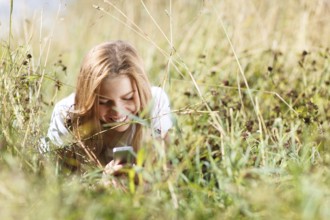 Beautiful girl is lying in the grass and writing sms on the phone in the city park at summer