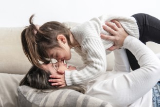 Mom and daughter are lying on the sofa, wearing white sweaters, sharing a tender moment of love and